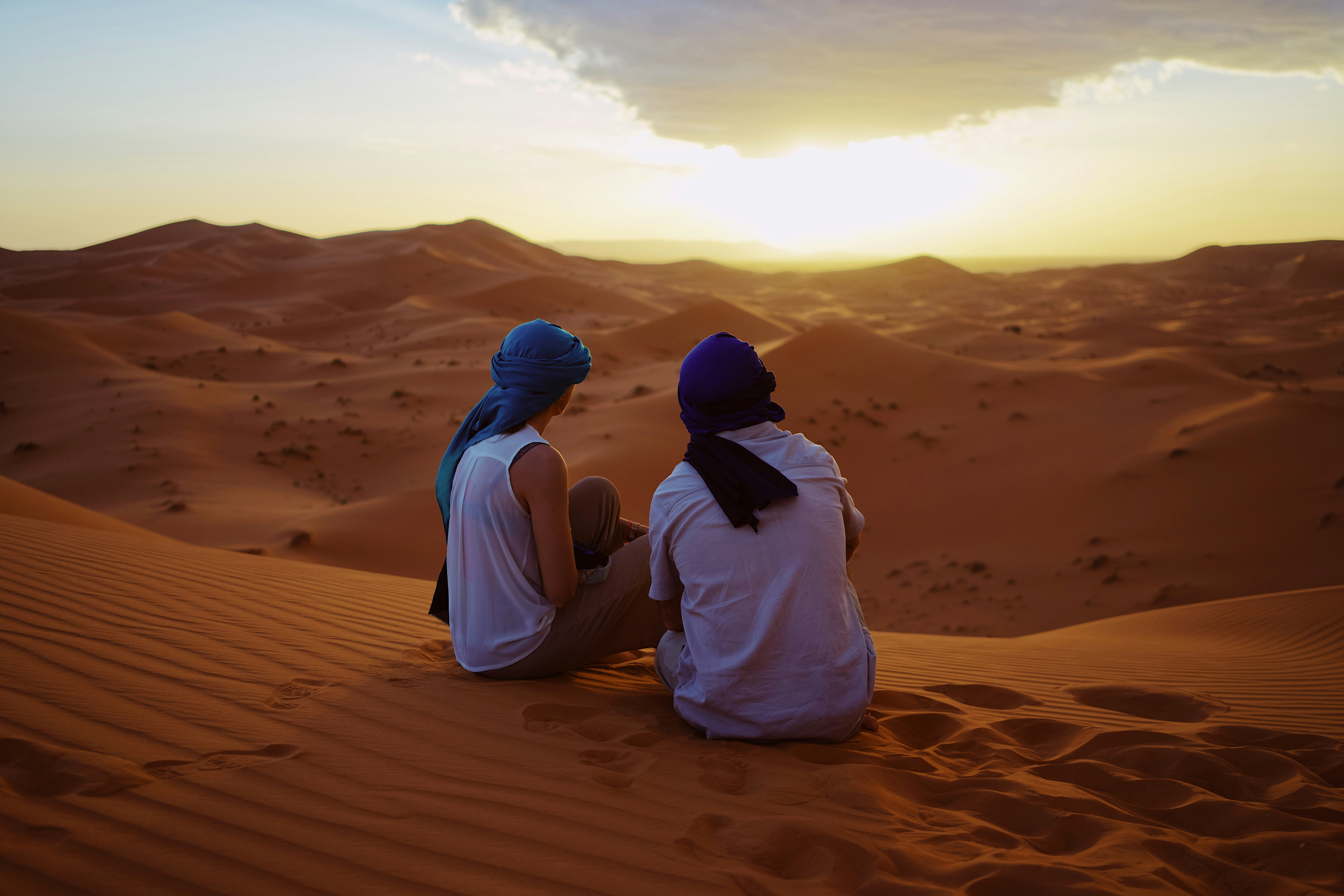 Two travellers watching the sunset over the dunes